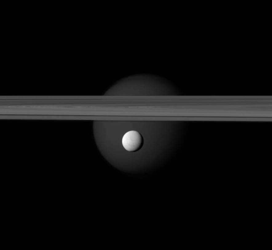 Enceladus, with its high reflective potential, is located in front of the planetary rings. Titan can be seen at a distance. At the south pole, there is an outburst of ice and steam from the water jets, indicating the presence of an underground sea. It is believed to contain organic matter and liquid hydrocarbons. Enceladus spans 504 km and is located in the middle. Titan covers 5150 km, but appears faint here because it is hidden behind a ring system. The image was taken in visible green light by the Cassini spacecraft's narrow-angle camera. The scale is 6 km per pixel. On March 12, 2012, the apparatus managed to approach 1 million km at an angle of 36 degrees. 