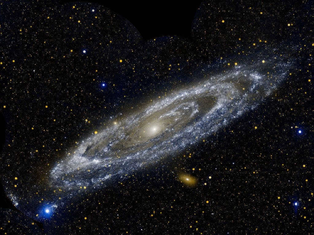 The GALEX telescope image shows the hot and bright stars of the Andromeda galaxy. It is the Milky Way's largest neighbor, stretching over 260000 light-years. This is such a huge space that 11 locations had to be imaged separately and joined together for the image. The white-blue lines forming galactic rings are areas where young and massive stars can be found. The dark blue ones mark cooled dust, where the formation of stars shrouded in dense cocoons is now evident. Eventually, they will be blown away by a powerful stellar wind. The white-orange ball in the center is a group of cooler and older stars. When viewed in visible light, the rings appear to be spiral arms. But in ultraviolet, the true structure is visible, also observed in Spitzer's infrared wavelengths. This proves that it was once in contact with M32 (over 200 million years ago). Andromeda is so bright that it is one of only 10 galaxies captured by an observer with the naked eye. The blue color represents ultraviolet light and the orange color represents near ultraviolet light