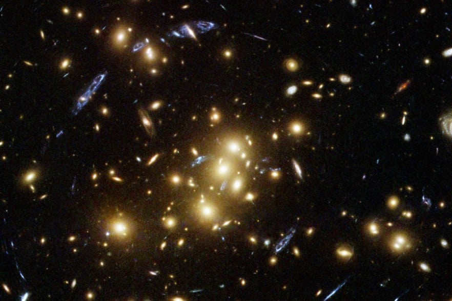 CL 0024+1654, imaged by Hubble in November 2004. The distinctive shape of the background forming galaxy allowed scientists to understand that it has separate images at 4, 10, 11, and 12 hours from the center of the cluster. The blue spot near the center is another image of the same galaxy. In a recent analysis, they found that 33 images of 11 separate galaxies can be distinguished.