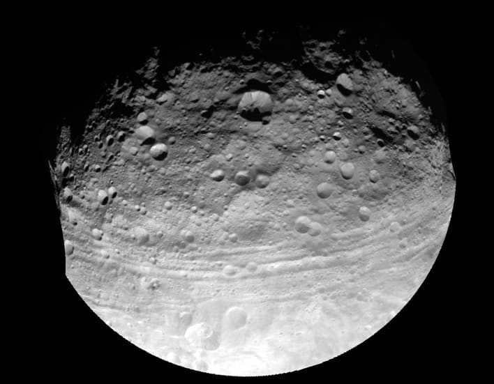 The giant asteroid Vesta is imaged by the Dawn spacecraft. A huge number of impact craters are visible on the surface.