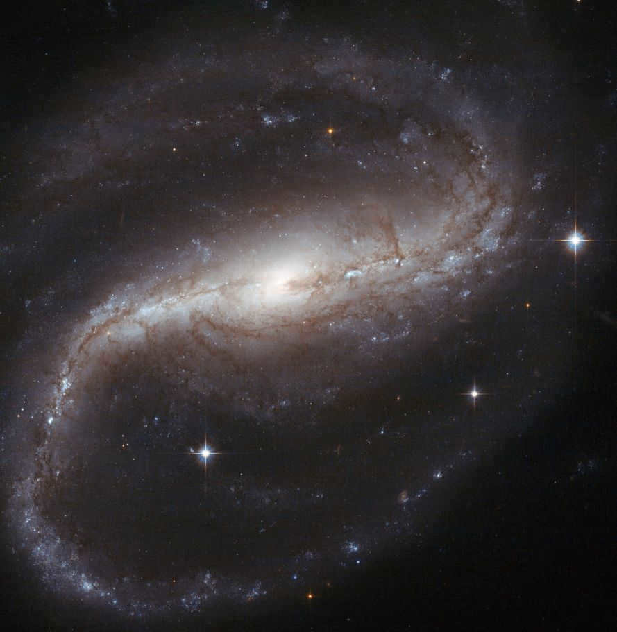 Galaxy NGC 7479 has been observed at visible and near-infrared wavelengths. The arms create an "S" when rotating in a counterclockwise direction. But in radio waves, it spins in the opposite direction, with a jet of radiation bending in the opposite direction to the stars and dust in the galaxy's shoulders. Scientists believe it's all about a merger with another galaxy in the past.