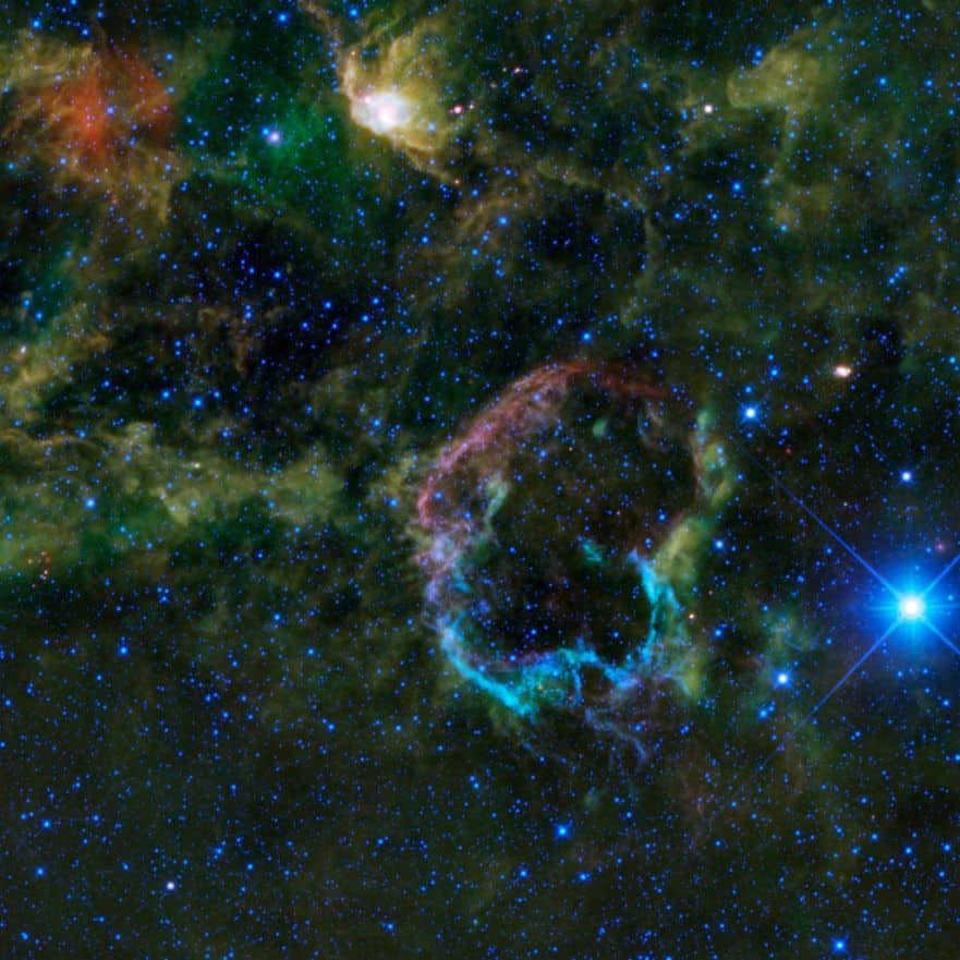 IC 443 is remarkable because the envelope is split into two halves that differ in radius, structure, and emission. The northeastern one is larger and displayed in purple color (upper left corner). It is represented by sheet-like filaments emitting light from neon, iron, silicon, oxygen atoms, and dust particles heated by the explosion. The southern side (bright blue below) is created by denser clumps and knots emitting light from hydrogen gas and heated dust.