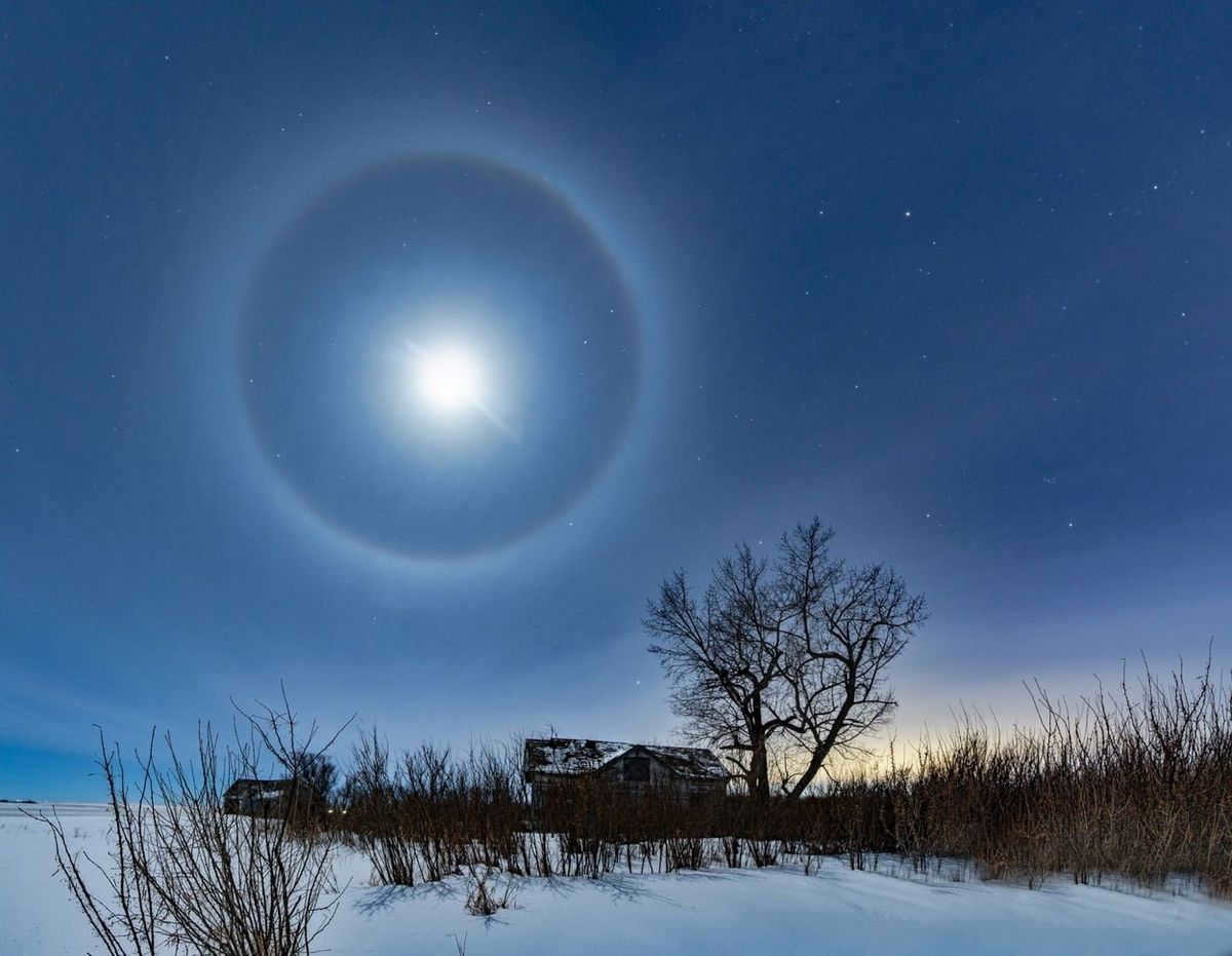In winter, a lunar halo shines over a farmhouse